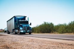 Blue semi-truck driving on a rural highway under clear blue skies